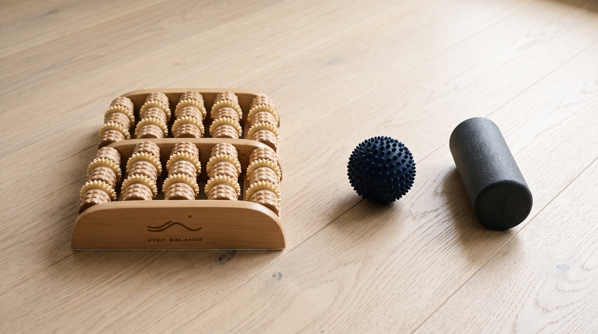 Step Balance ReflexRoll wooden foot roller next to a spiky massage ball and a small foam roller on an oak floor