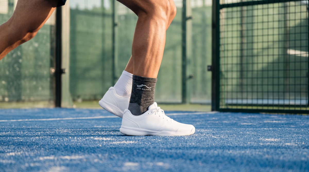 Padel player’s lower leg in a gray knit ankle sleeve and padel shoe, mid split-step on a blue artificial-grass court